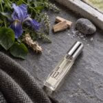 Green Irish Tweed decant resting on slate beside iris, green leaves and tweed